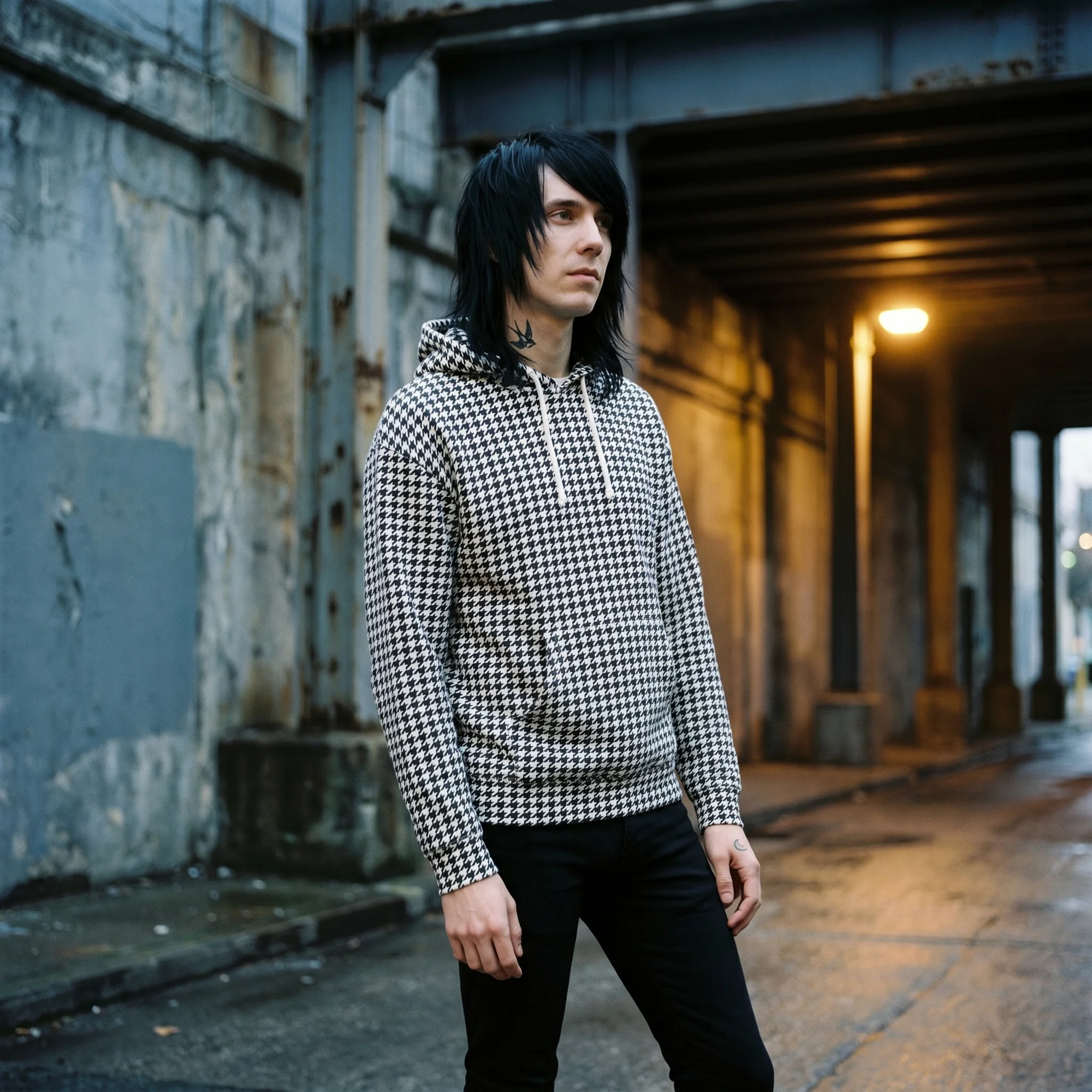 Man wearing a black and white houndstooth hoodie, front view, hood down, in a moody industrial setting
