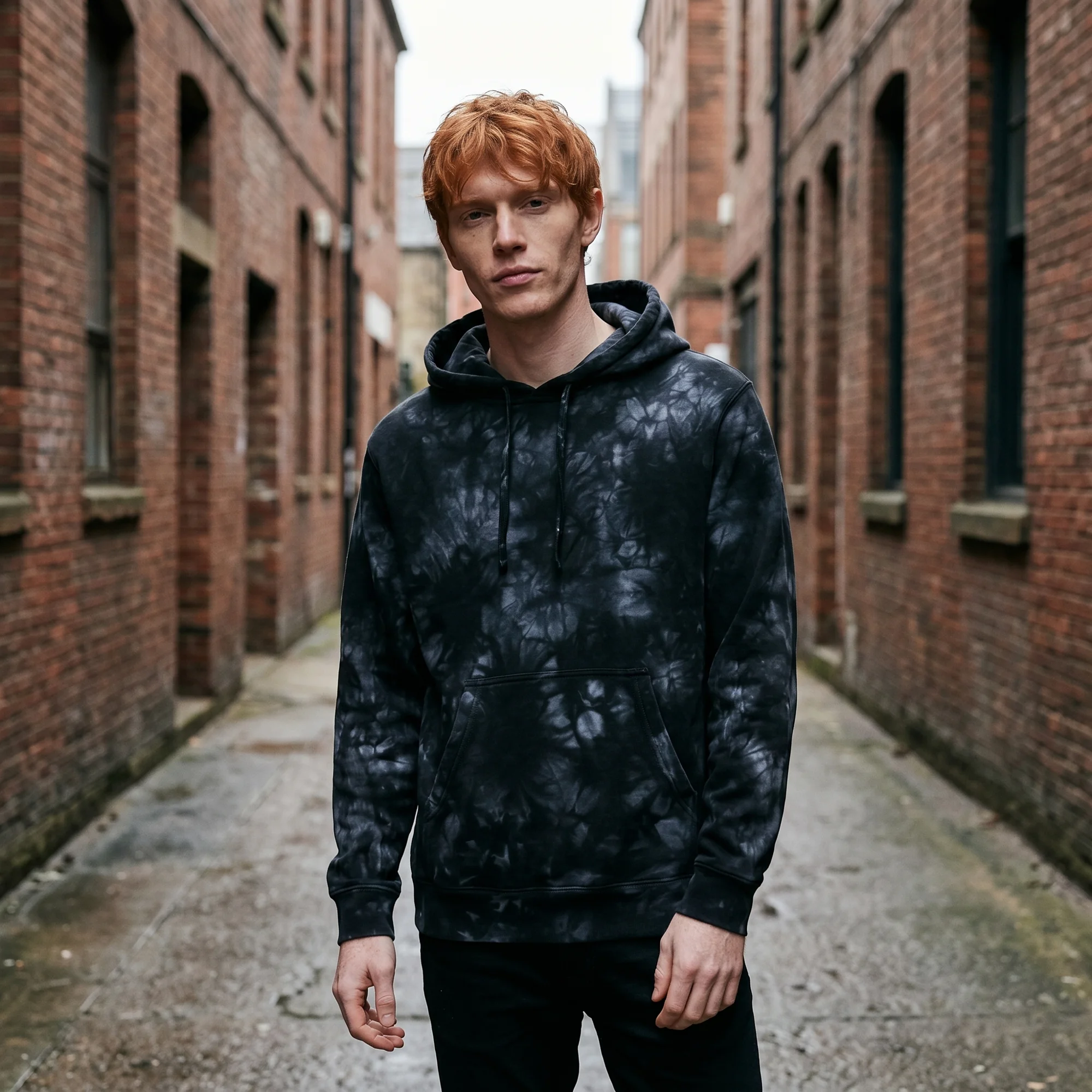 Man wearing an black tie-dye hoodie, front view, hood down, in a brick alley