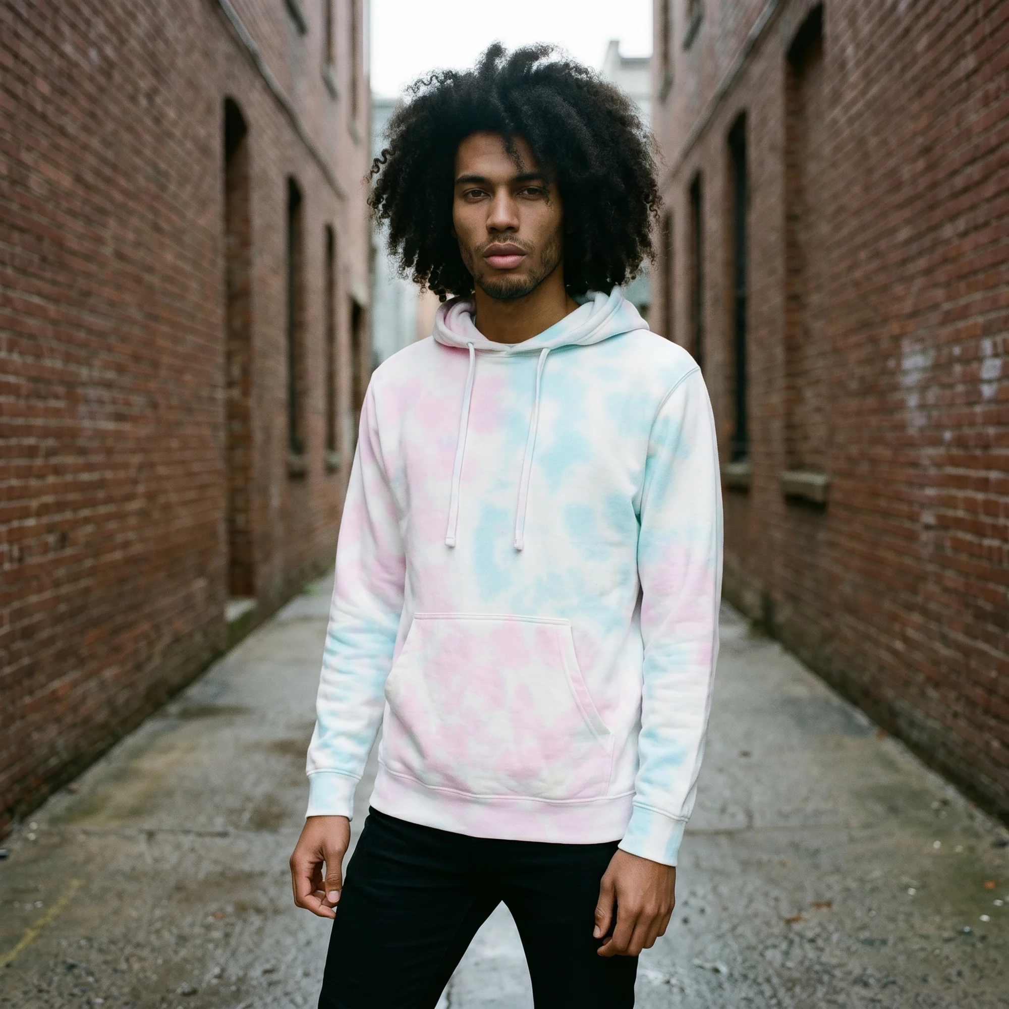 Man wearing an cotton candy tie-dye hoodie, front view, hood down, in a brick alley