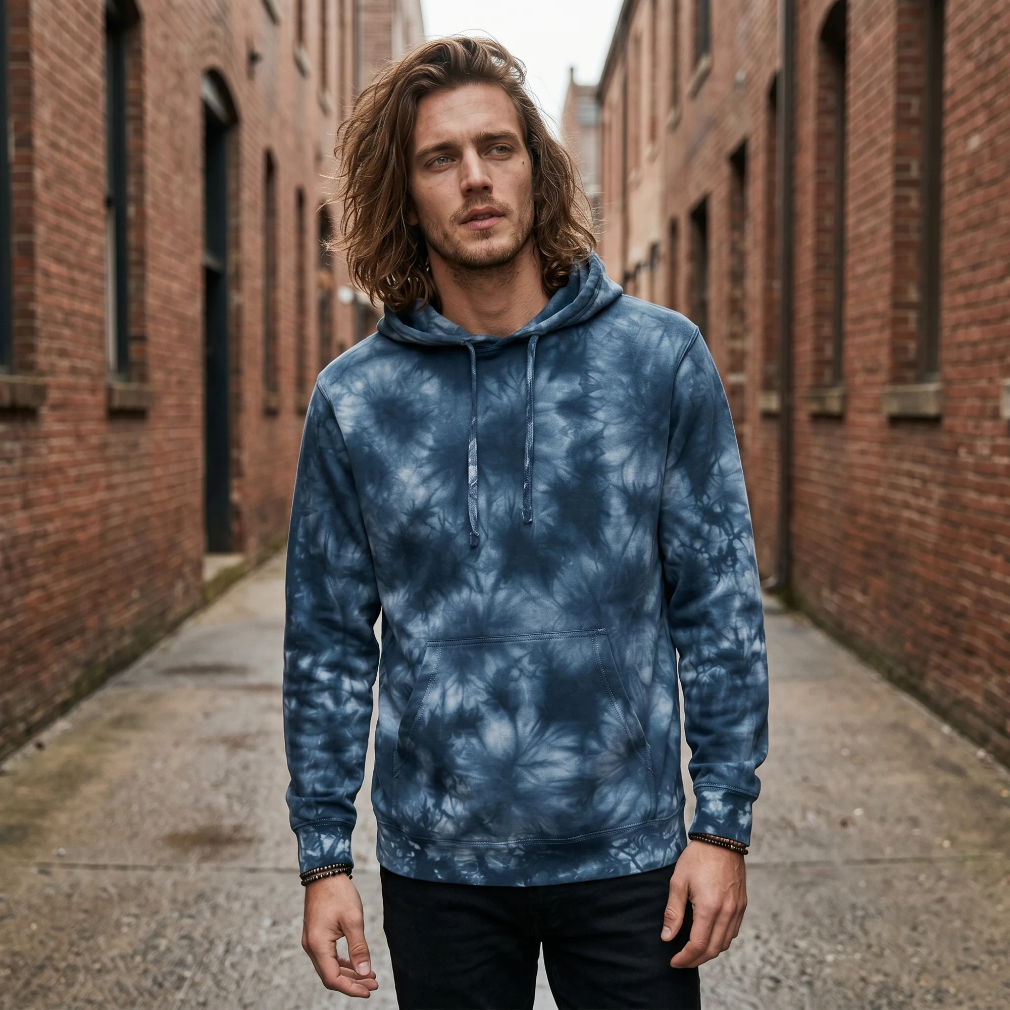 Man wearing an navy tie-dye hoodie, front view, hood down, in a brick alley