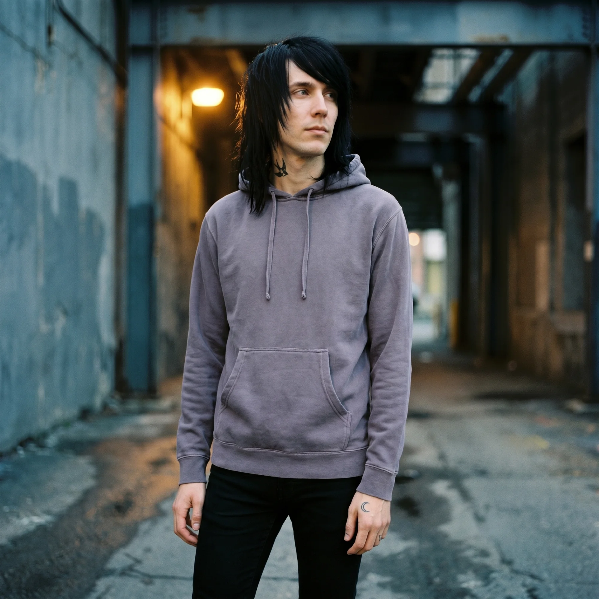 Man wearing a plum pigment dye hoodie, front view, hood down, in a moody industrial setting