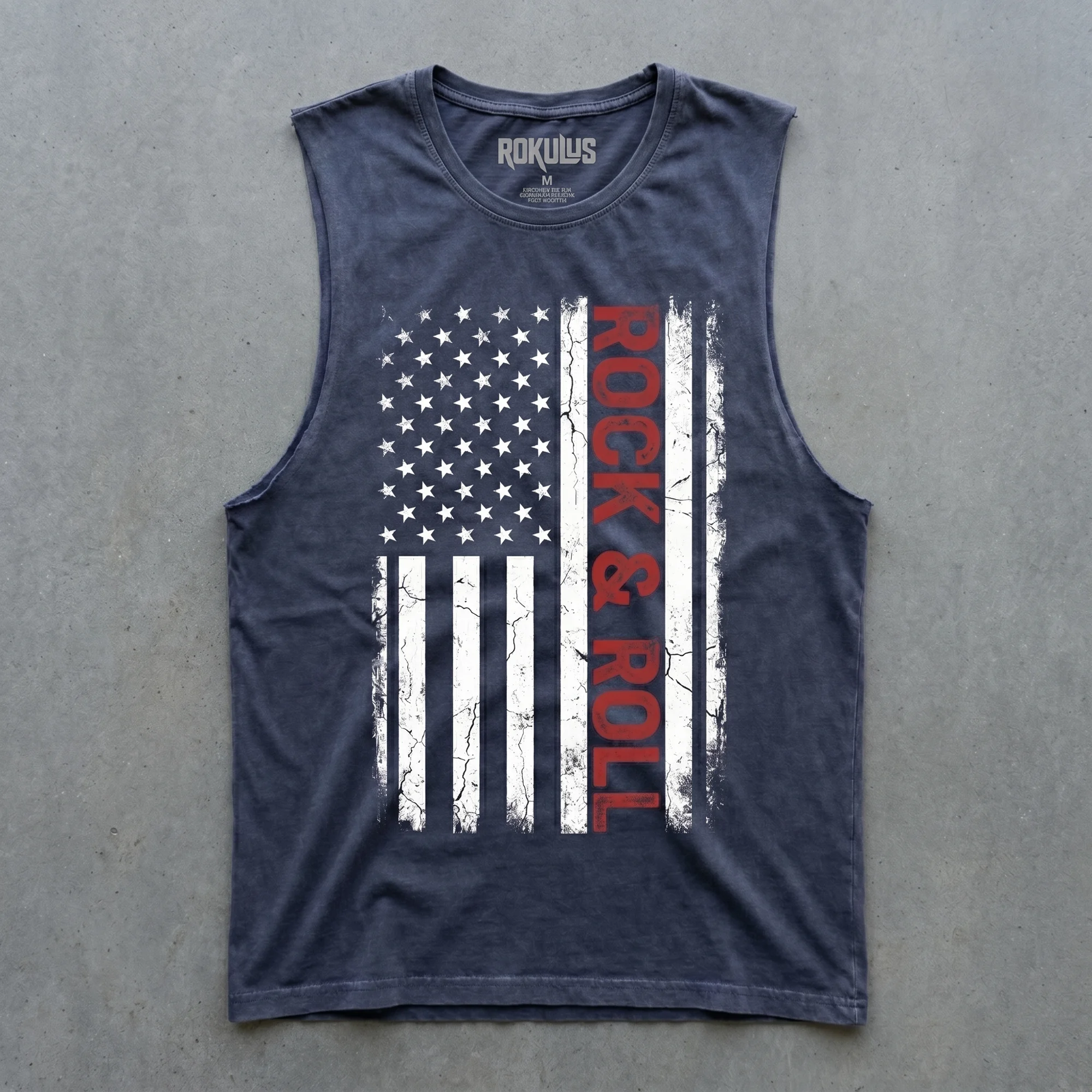 Blue stone wash tank top laid flat on concrete, showing the weathered American flag graphic with vertical "Rock & Roll" lettering and the Rokulus inner-neck label