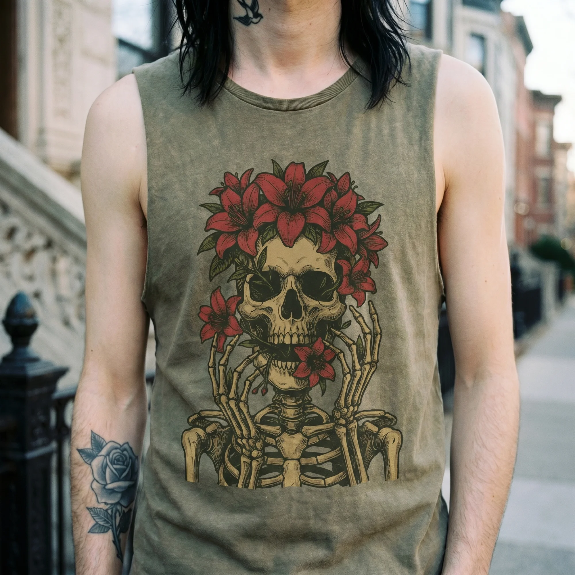 Close-up front view of a man wearing a moss green tank top with the vintage tattoo-flash floral skull graphic — skull crowned with red lilies and skeletal hands