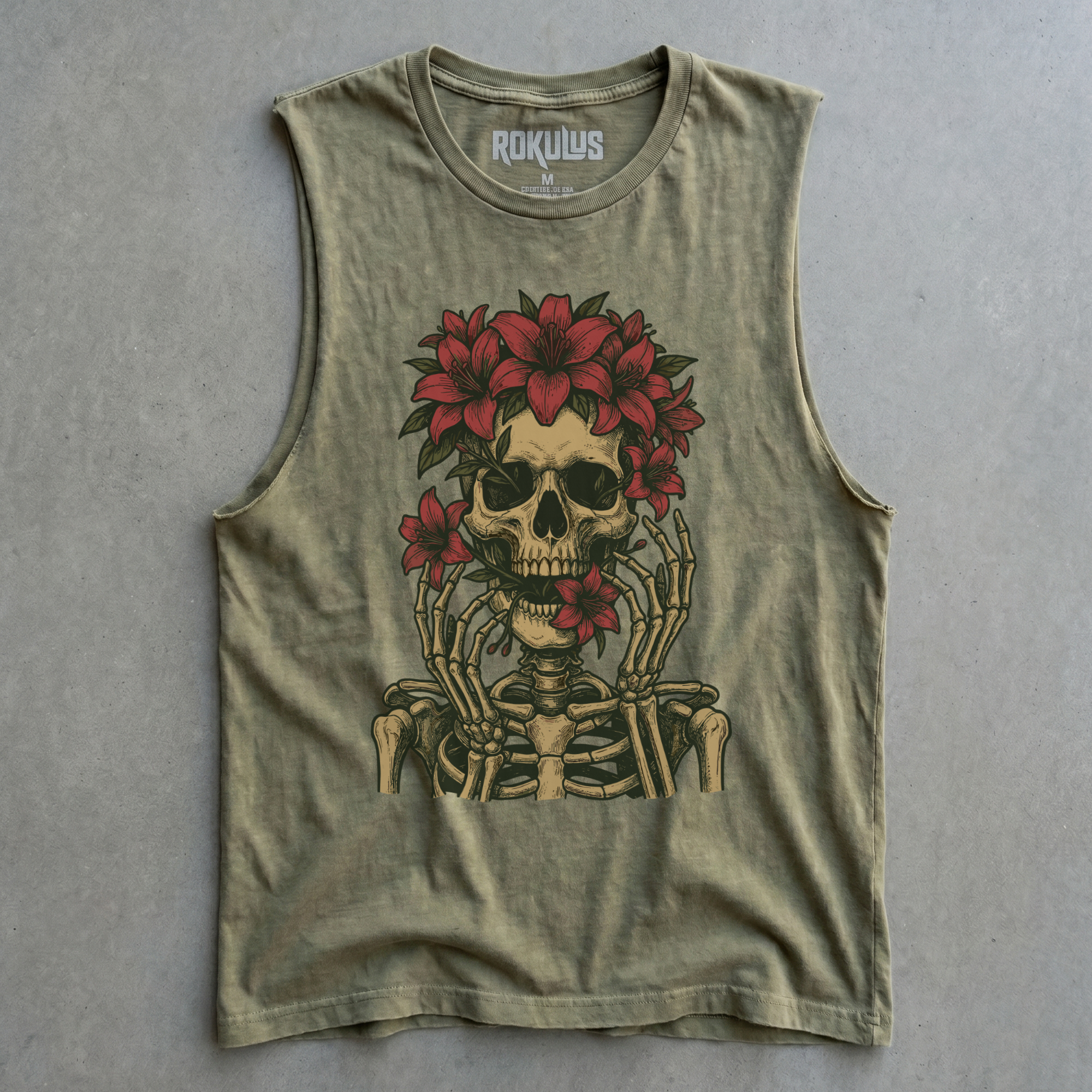 Moss green cut-off muscle tank laid flat on concrete, showing the floral skull graphic with red lilies and skeletal hands, plus the Rokulus inner-neck label