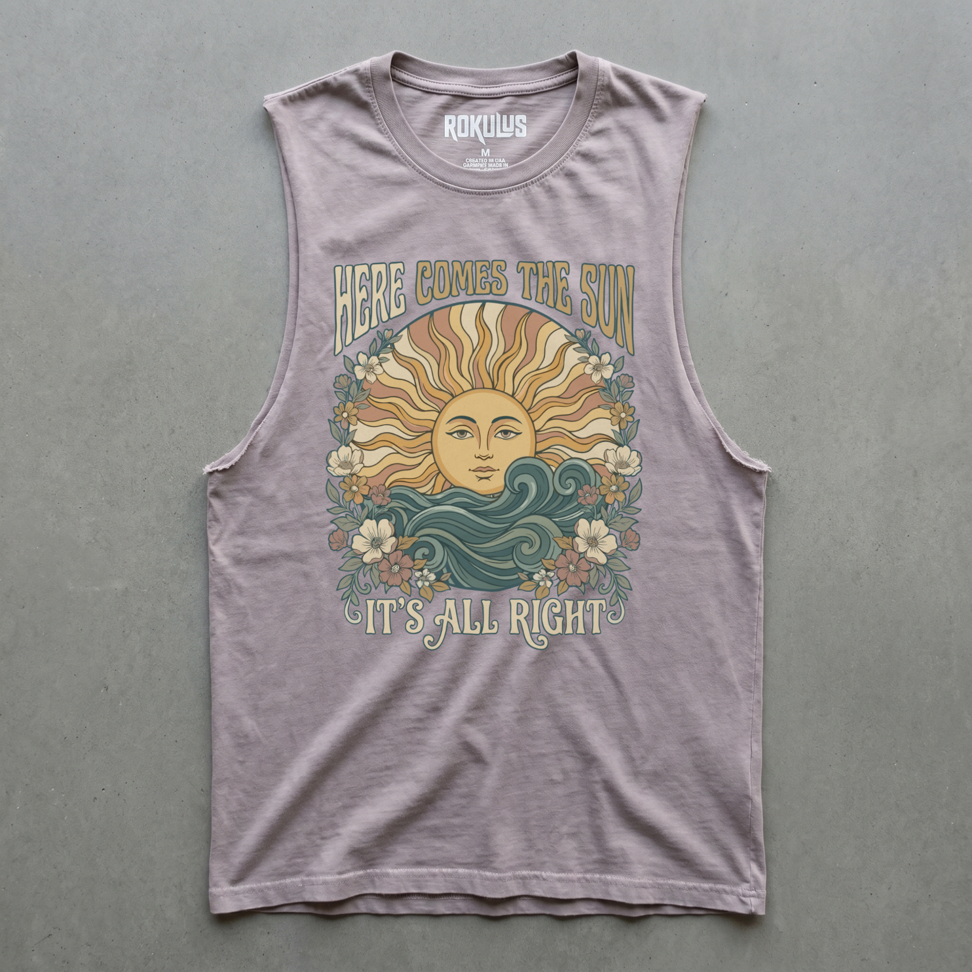 Orchid cut-off muscle tank laid flat on concrete, showing the Here Comes the Sun sun-and-florals graphic with "Here Comes the Sun / It's All Right" lettering, plus the Rokulus inner-neck label