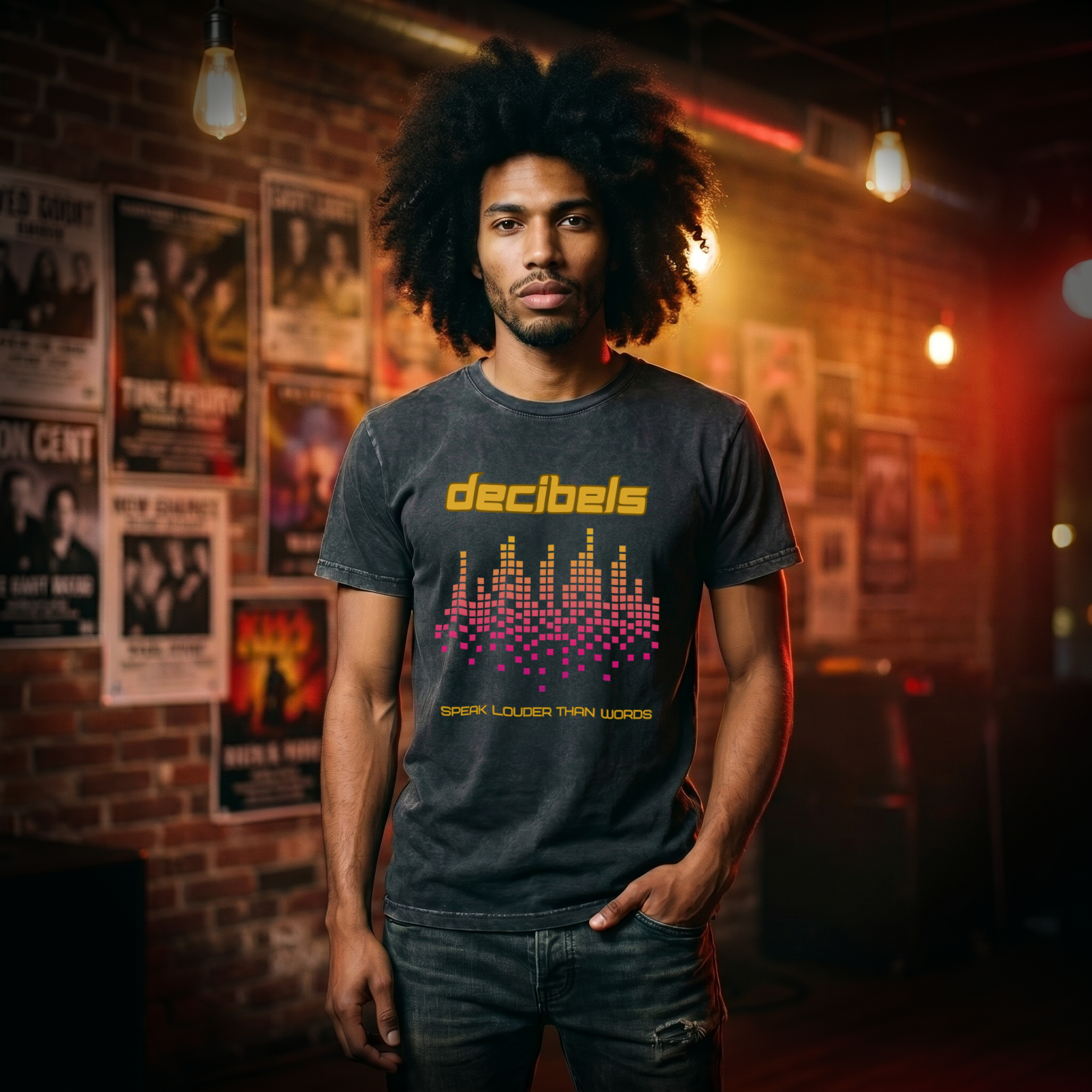 Man wearing a black vintage wash t-shirt with a yellow Decibels graphic and pink-orange equalizer, front view, in a moody music venue with gig posters