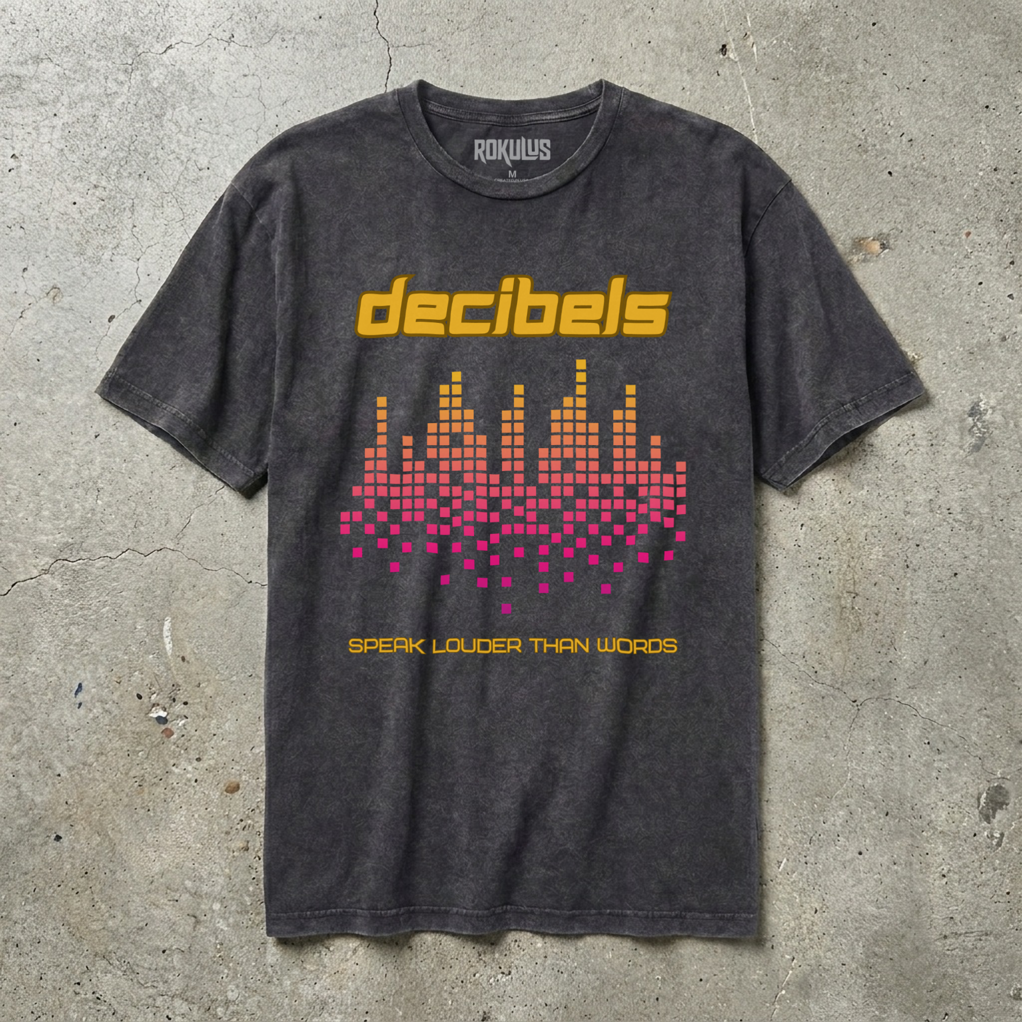 Black vintage wash t-shirt laid flat on concrete, showing the Decibels equalizer graphic in yellow, orange, and pink