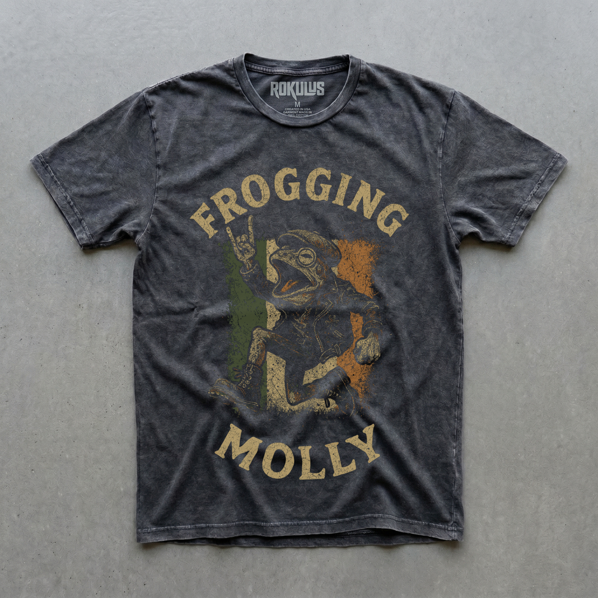Black vintage wash t-shirt laid flat on concrete, showing the Frogging Molly Celtic punk frog graphic in cream, green, and orange over the Irish tricolor