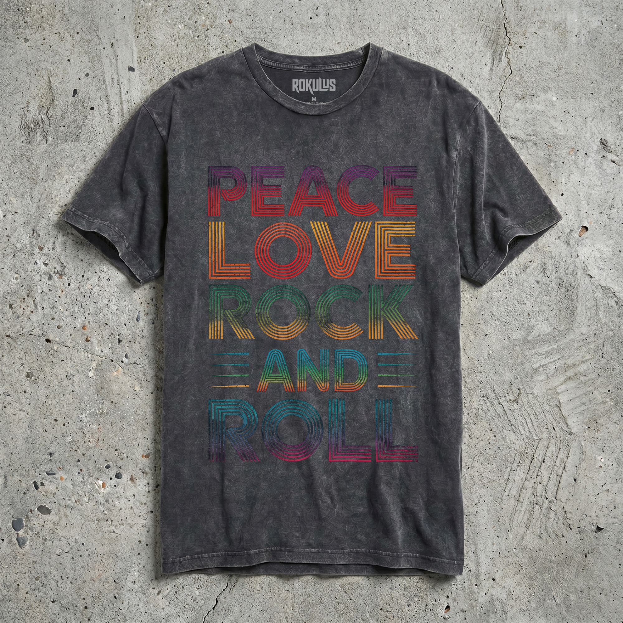 Black vintage wash t-shirt laid flat on concrete, showing the Peace Love Rock and Roll rainbow retro typography graphic