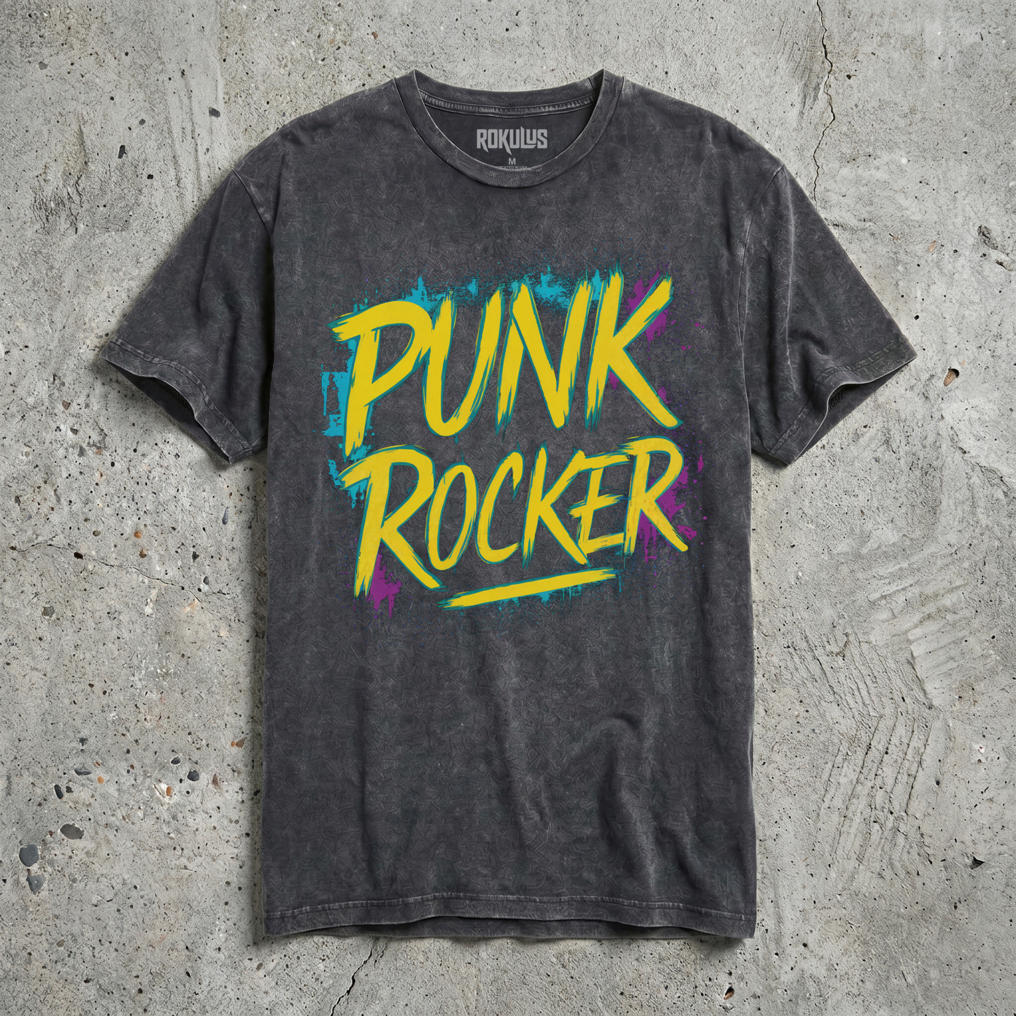 Black vintage wash t-shirt laid flat on concrete, showing the Punk Rocker yellow graffiti typography with cyan and magenta paint splatter