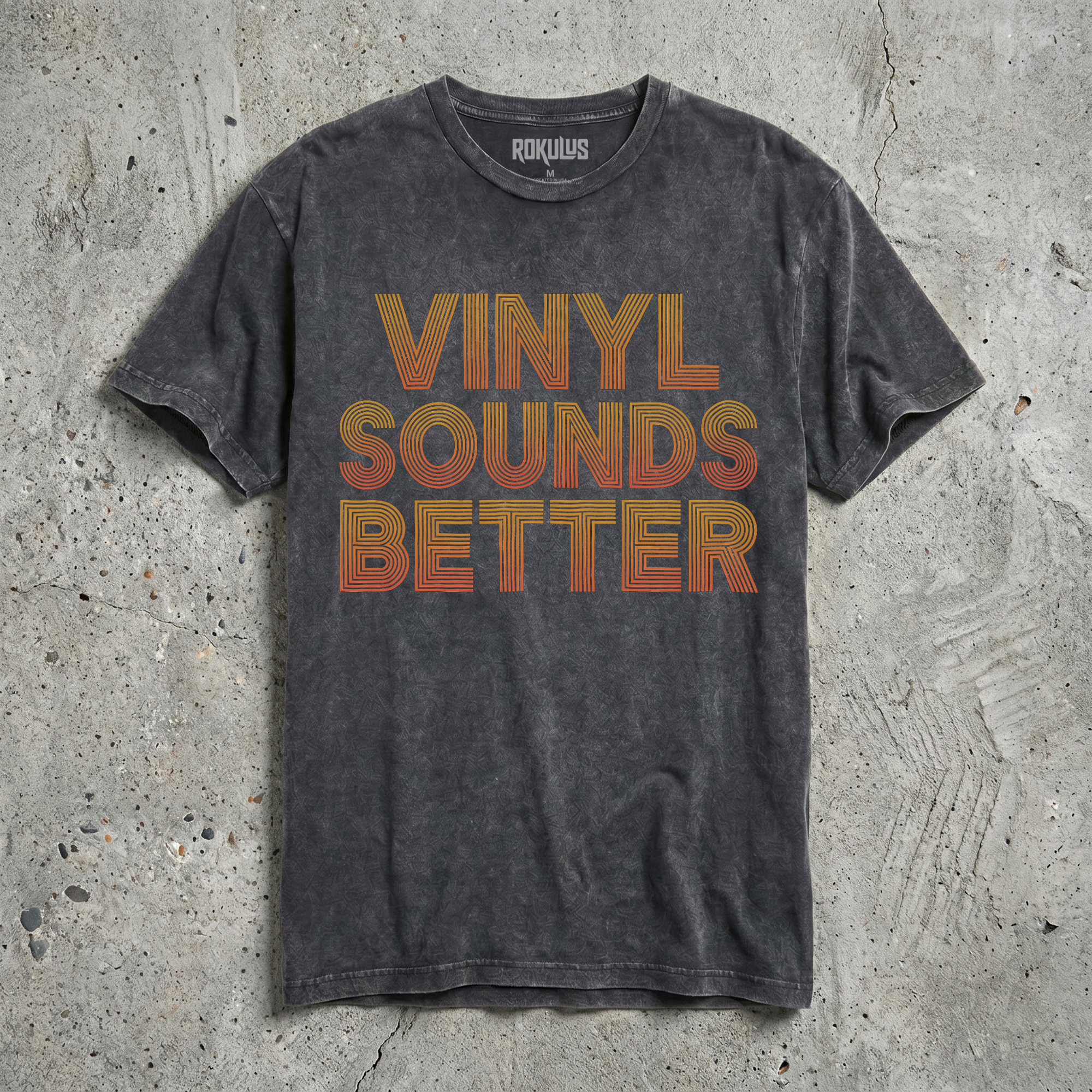 Black vintage wash t-shirt laid flat on concrete, showing the Vinyl Sounds Better retro 70s typography graphic in golden orange