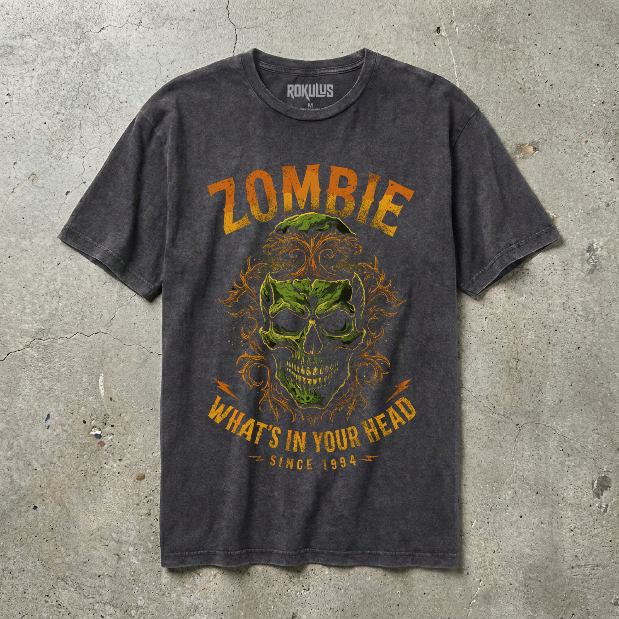 Black vintage wash t-shirt laid flat, showing the zombie skull horror graphic in green, orange, and gold