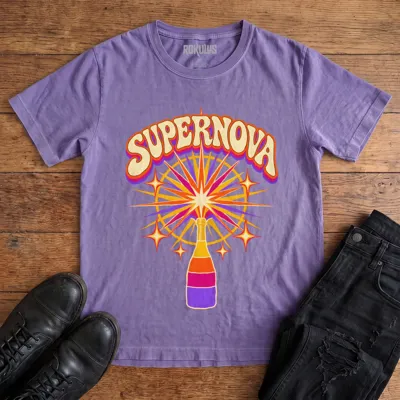 Washed purple Rokulus Champagne Supernova vintage graphic tee laid flat on wood with black boots and jeans, front print showing a champagne bottle erupting in a psychedelic sunburst of purple, pink, and orange under groovy “Supernova” lettering