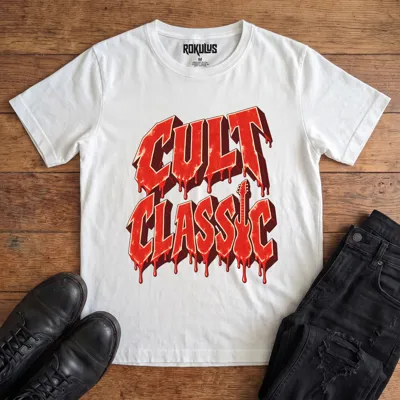 White Rokulus Cult Classic vintage graphic tee laid flat on wood with black boots and jeans, front print showing “Cult Classic” in dripping blood-red horror-movie lettering with a guitar silhouette forming the letter I