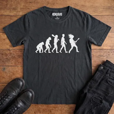 Washed black Rokulus Rock Evolution vintage graphic tee laid flat on wood with black boots and jeans, front print showing the evolution chart silhouette ending in a long-haired rocker shredding an electric guitar