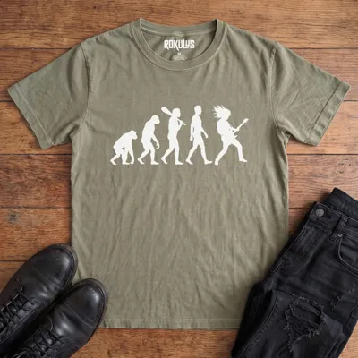 Washed olive Rokulus Rock Evolution vintage graphic tee laid flat on wood with black boots and jeans, front print showing the evolution chart silhouette ending in a long-haired rocker shredding an electric guitar