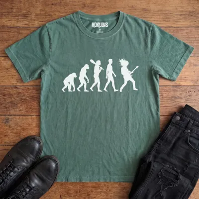 Washed pine Rokulus Rock Evolution vintage graphic tee laid flat on wood with black boots and jeans, front print showing the evolution chart silhouette ending in a long-haired rocker shredding an electric guitar