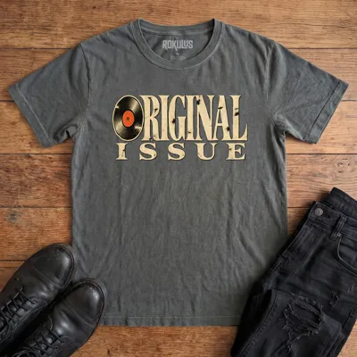 Washed charcoal Rokulus Original Issue vintage graphic tee laid flat on wood with black boots and jeans, front print showing “Original Issue” in distressed vintage serif lettering with a vinyl record forming the letter O