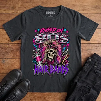 Washed black Rokulus Raised On 80s Hair Bands vintage graphic tee laid flat on wood with black boots and jeans, front print showing a big-haired skeleton glam rocker in star sunglasses with hairspray, drumsticks, and animal print in neon and chrome