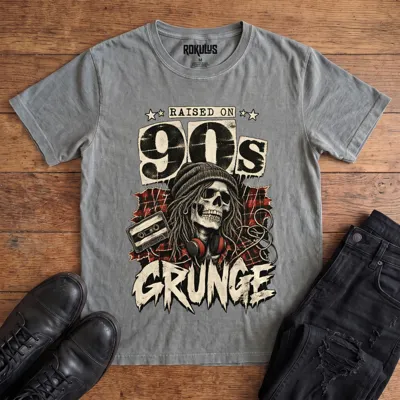 Washed grey Rokulus Raised On 90s Grunge vintage graphic tee laid flat on wood with black boots and jeans, front print showing a long-haired skull in a beanie and headphones on red plaid flannel with a cassette tape under “Raised On 90s Grunge” lettering