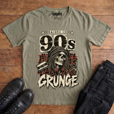 Washed olive Rokulus Raised On 90s Grunge vintage graphic tee laid flat on wood with black boots and jeans, front print showing a long-haired skull in a beanie and headphones on red plaid flannel with a cassette tape under “Raised On 90s Grunge” lettering