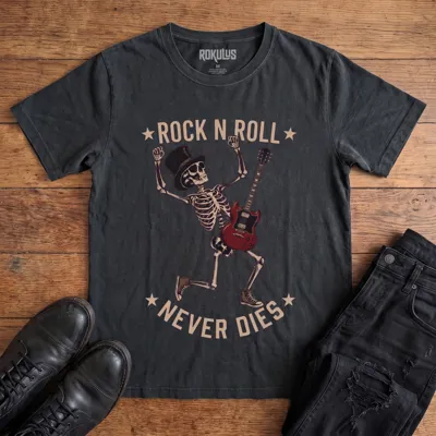 Washed black Rokulus Rock N Roll Never Dies vintage graphic tee laid flat on wood with black boots and jeans, front print showing a dancing top-hat skeleton with a red electric guitar and fists raised under arched "Rock N Roll Never Dies" lettering