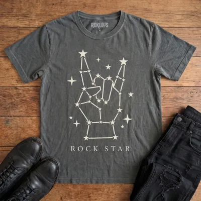 Washed charcoal Rokulus Rock Star Constellation vintage graphic tee laid flat on wood with black boots and jeans, front print showing a rock horns hand formed from a star constellation above “Rock Star” lettering in cream