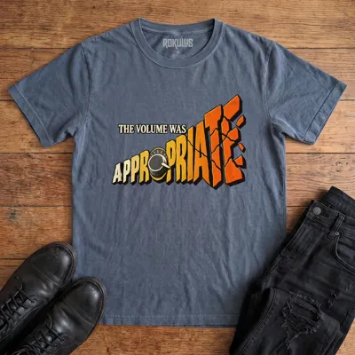 Washed navy blue Rokulus The Volume Was Appropriate vintage graphic tee laid flat on wood with black boots and jeans, front print reading “The Volume Was Appropriate” with a cranked amp knob and shattering orange-to-yellow lettering