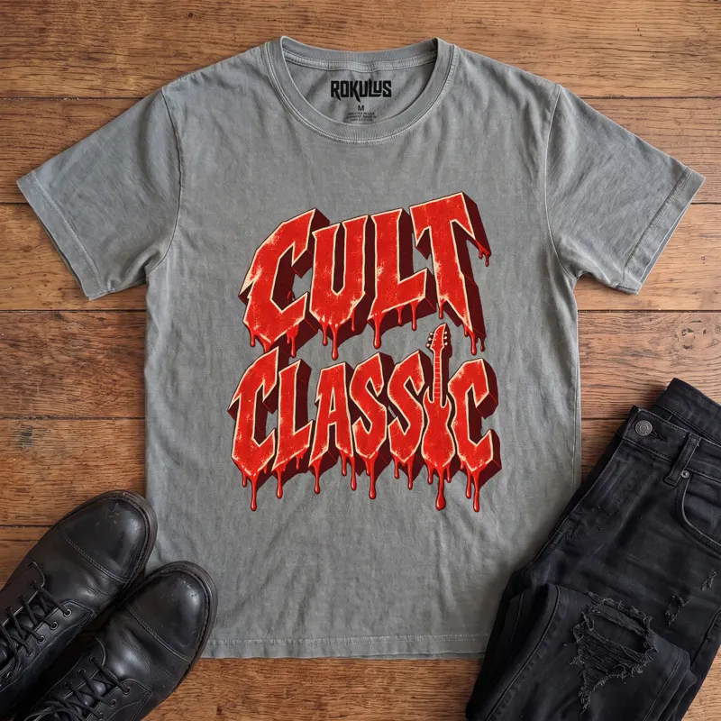 Washed grey Rokulus Cult Classic vintage graphic tee laid flat on wood with black boots and jeans, front print showing “Cult Classic” in dripping blood-red horror-movie lettering with a guitar silhouette forming the letter I
