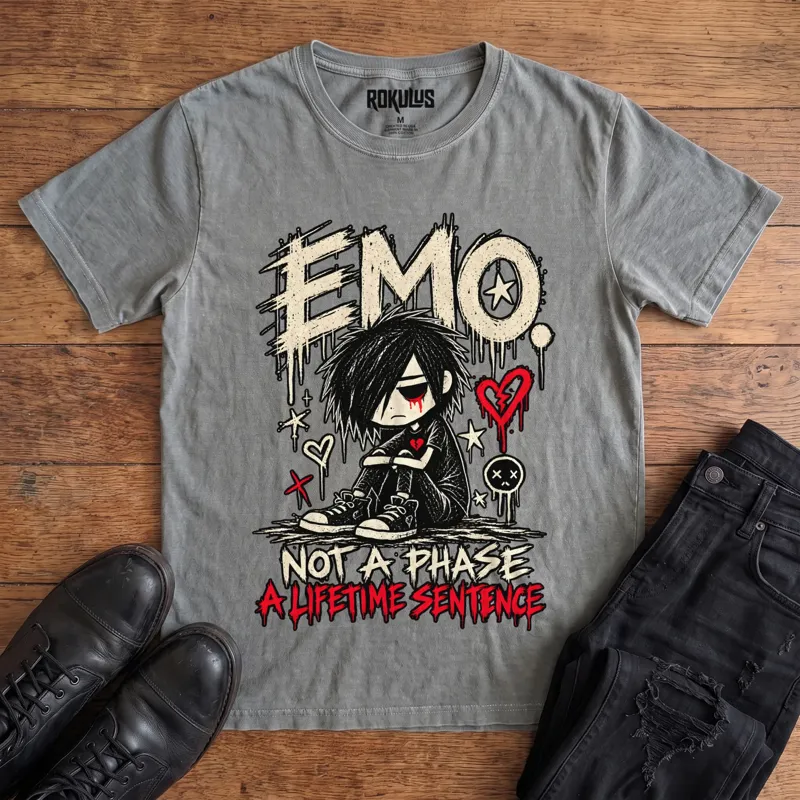 Washed grey Rokulus Emo Not A Phase vintage graphic tee laid flat on wood with black boots and jeans, front print showing a moody emo kid hugging his knees under dripping “Emo” lettering with broken hearts and “Not A Phase, A Lifetime Sentence”