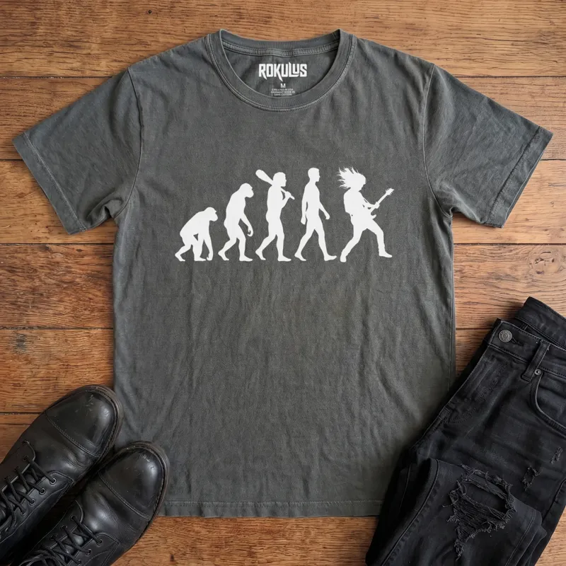 Washed charcoal Rokulus Rock Evolution vintage graphic tee laid flat on wood with black boots and jeans, front print showing the evolution chart silhouette ending in a long-haired rocker shredding an electric guitar