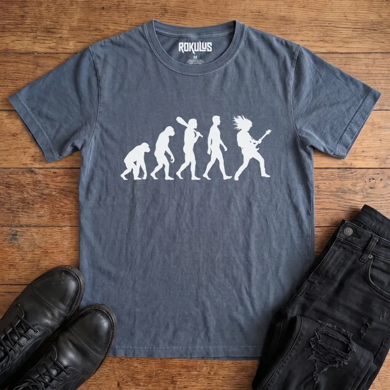 Washed navy Rokulus Rock Evolution vintage graphic tee laid flat on wood with black boots and jeans, front print showing the evolution chart silhouette ending in a long-haired rocker shredding an electric guitar