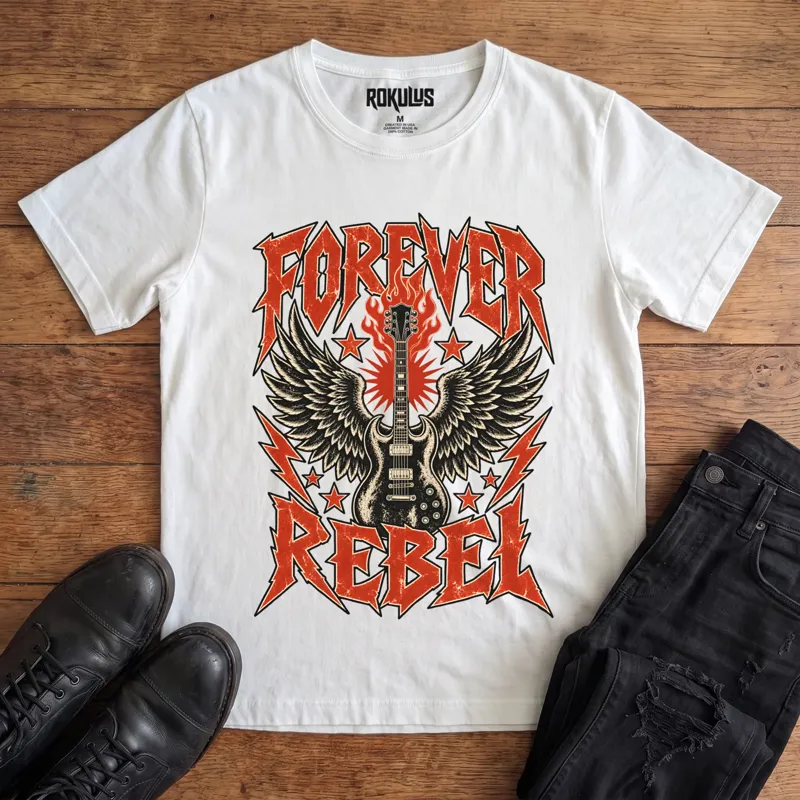 White Rokulus Forever Rebel vintage graphic tee laid flat on wood with black boots and jeans, front print showing a winged electric guitar in flames with lightning bolts and stars under jagged “Forever Rebel” metal lettering