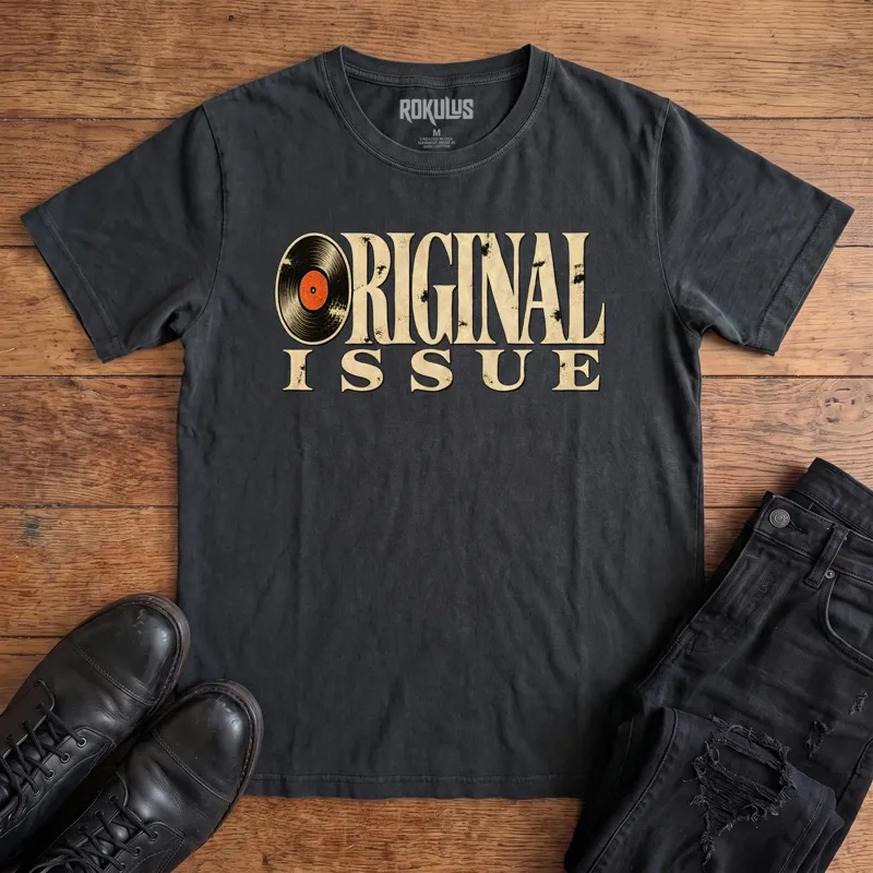 Washed black Rokulus Original Issue vintage graphic tee laid flat on wood with black boots and jeans, front print showing “Original Issue” in distressed vintage serif lettering with a vinyl record forming the letter O