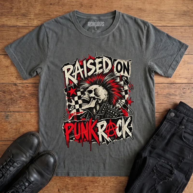 Washed charcoal Rokulus Raised On Punk Rock vintage graphic tee laid flat on wood with black boots and jeans, front print showing a red-mohawked screaming skull in a studded jacket with safety pins, checkerboard, and an anarchy symbol under “Raised On Punk Rock” lettering