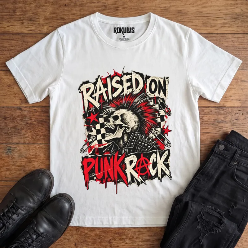 White Rokulus Raised On Punk Rock vintage graphic tee laid flat on wood with black boots and jeans, front print showing a red-mohawked screaming skull in a studded jacket with safety pins, checkerboard, and an anarchy symbol under “Raised On Punk Rock” lettering