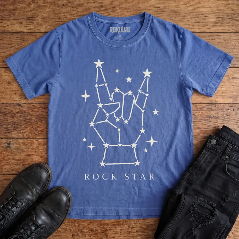 Washed royal blue Rokulus Rock Star Constellation vintage graphic tee laid flat on wood with black boots and jeans, front print showing a rock horns hand formed from a star constellation above “Rock Star” lettering in cream