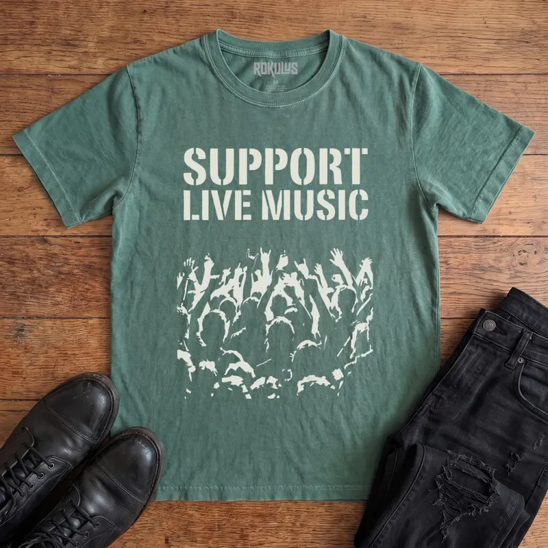 Washed pine Rokulus Support Live Music vintage graphic tee laid flat on wood with black boots and jeans, front print showing "Support Live Music" in stencil type above a silhouetted concert crowd with raised hands